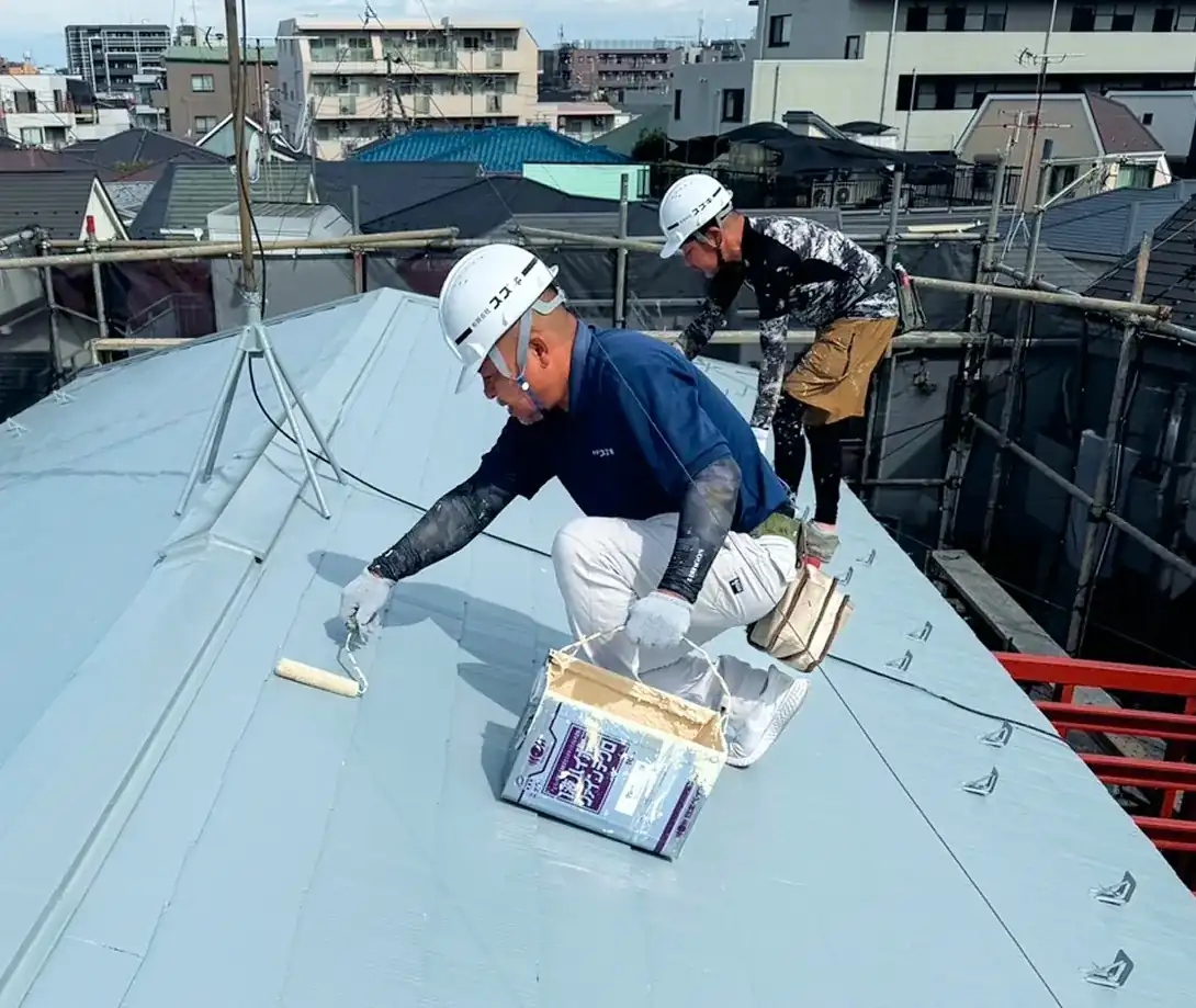 都会の屋根の上で、丁寧に塗料を塗る作業。職人たちの集中力と技術が光る瞬間。